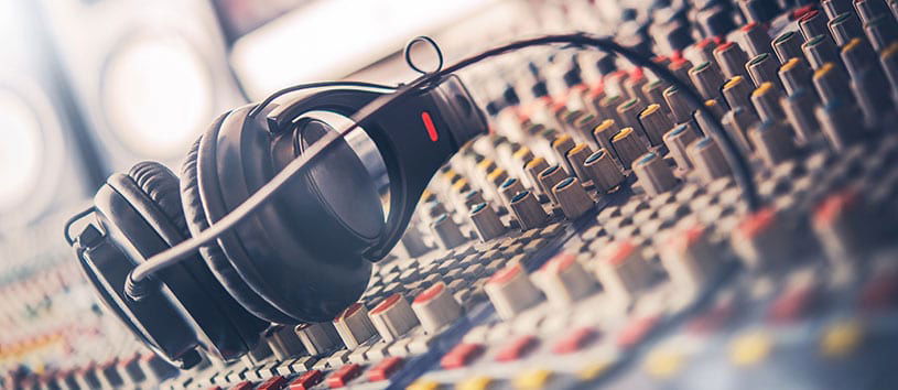 Pair of headphones sit on a mixing baord in a radio broadcast studio
