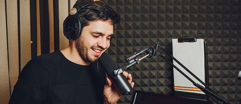 Man speaks into microphone in sound-proofed radio studio.